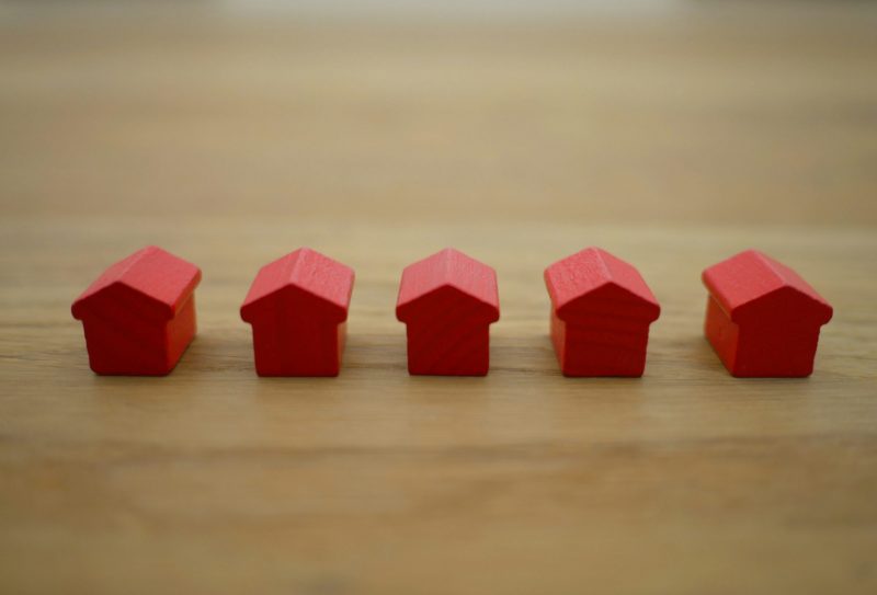 6 red wooden monopoly house pieces lined up in a tidy row on a wooden desk